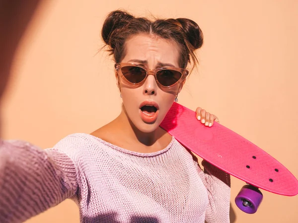 サングラスをかけた若い美しいセクシーな笑顔のヒップスター女性 夏のニットカーディガンでトレンディな女の子 ピンクのペニースケートボードを持つ女性 上に隔離 — ストック写真