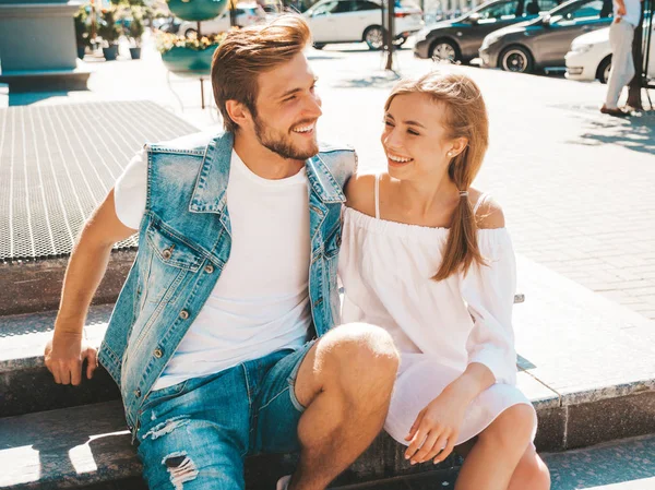 Gülümseyen güzel kız ve onun yakışıklı erkek arkadaşı. Rahat yazlık elbiseli kadın ve kot pantolon giyen bir erkek. Mutlu neşeli bir aile. Sokak arka planında merdivenlerde oturuyorum. Sarılan çift