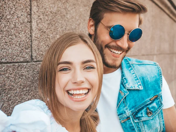 Gündelik kıyafetlerle gülümseyen güzel bir kız ve yakışıklı erkek arkadaşı. Mutlu bir aile, güneş gözlükleriyle kendi fotoğraflarını çekiyor. Duvarın yanındaki sokakta eğleniyorlar. 