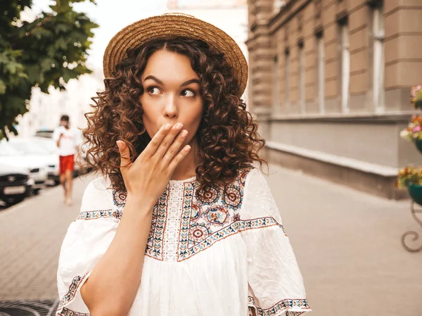 Beautiful smiling model with afro curls hairstyle dressed in summer hipster white dress.Sexy carefree girl posing in the street.Shocked and surprised woman.Hand near mouth