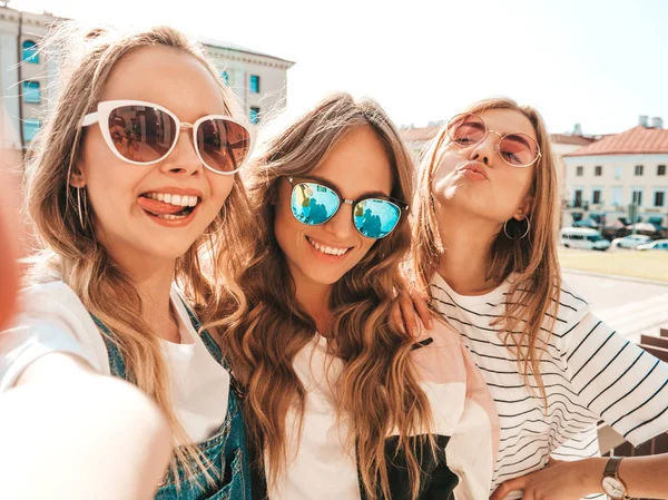 夏服を着た3人の若い笑顔のヒップスター女性 スマートフォンで自分撮りセルフポートレート写真を撮る女の子 路上でポーズをとるモデル サングラスでポジティブな顔の感情を示す女性 — ストック写真