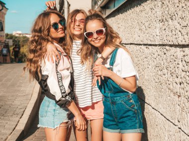 Moda yazlık giysiler üç genç güzel gülümseyen hipster kız Portresi. Seksi kaygısız kadınlar duvara yakın sokakta poz. Güneş gözlüğü ile eğlenen pozitif modeller. Sarılma