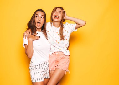 Trendy yaz giysileri iki genç güzel gülümseyen hipster kız. Seksi kaygısız kadınlar stüdyoda sarı duvar yakınında poz. Pozitif modeller deli gidiyor ve eğleniyor. Sarılma