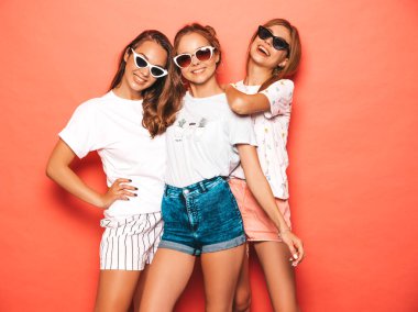 Moda yazlık giysiler üç genç güzel gülümseyen hipster kız. Seksi kaygısız kadınlar stüdyoda pembe duvar yakınında poz. Pozitif modeller deli gidiyor ve eğleniyor. Güneş gözlüğü olarak