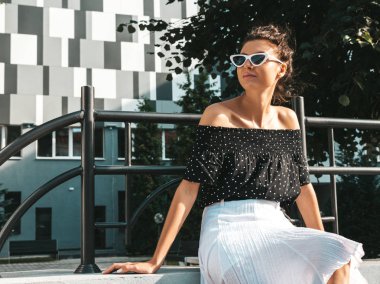 Zarif yazlık giysiler giymiş güzel gülümseyen model. Sokak arka planda oturan seksi kaygısız kız. Güneş gözlüğü trendy modern iş kadını eğlenmek