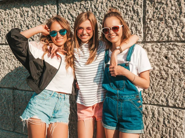 トレンディな夏の服を着た3人の若い美しい笑顔のヒップスターの女の子の肖像画 壁の近くの通りでポーズセクシーな気楽な女性 サングラスで楽しいポジティブなモデル 抱いて — ストック写真