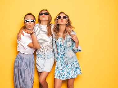 Moda yazlık giysiler üç genç güzel gülümseyen hipster kız. Seksi kaygısız kadınlar stüdyoda sarı duvar yakınında poz. Pozitif modeller deli gidiyor ve eğleniyor. Ördek surat yapma