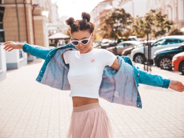 Boynuzları saç modeli yaz hipster ceket kot elbise giymiş ile bulanık güzel gülümseyen model. Seksi kaygısız kız sokak arka planda poz. Pozitif kadın güneş gözlüğü eğlenmek