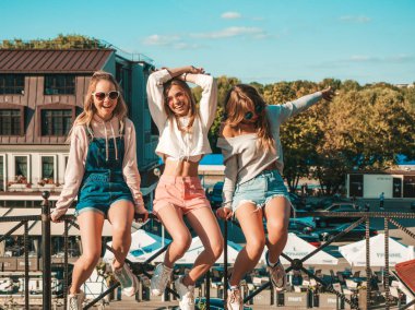 Moda yazlık giysiler üç genç güzel gülümseyen hipster kız Portresi. Sokakta ki tırabzanda oturan seksi kaygısız kadınlar. Güneş gözlüğü ile eğlenen pozitif modeller