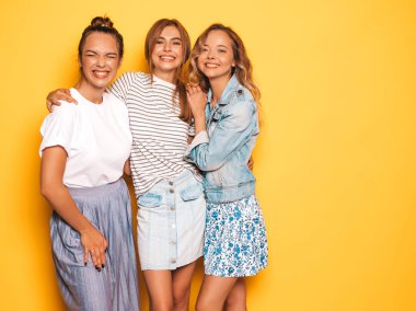 Moda yazlık giysiler üç genç güzel gülümseyen hipster kız. Seksi kaygısız kadınlar stüdyoda sarı duvar yakınında poz. Pozitif modeller deli gidiyor ve eğlenmek 