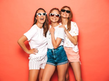 Moda yazlık giysiler üç genç güzel gülümseyen hipster kız. Seksi kaygısız kadınlar stüdyoda pembe duvar yakınında poz. Pozitif modeller deli gidiyor ve güneş gözlüğü eğlenmek