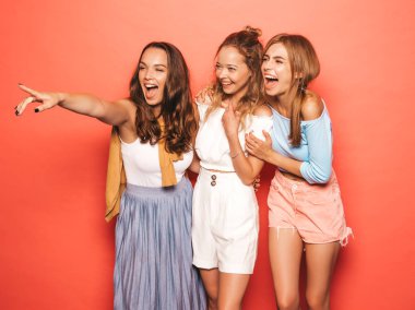 Moda yazlık giysiler üç genç güzel gülümseyen hipster kız. Seksi kaygısız kadınlar stüdyoda pembe duvar yakınında poz. Pozitif modeller deli gidiyor ve eğleniyor. Mağaza satışlarına işaret etmek