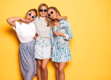 Moda yazlık giysiler üç genç güzel gülümseyen hipster kız. Seksi kaygısız kadınlar stüdyoda sarı duvar yakınında poz. Pozitif modeller deli gidiyor ve eğlenmek 