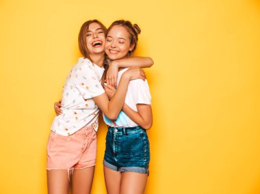 Trendy yaz giysileri iki genç güzel gülümseyen hipster kız. Seksi kaygısız kadınlar stüdyoda sarı duvar yakınında poz. Pozitif modeller deli gidiyor ve eğleniyor. Sarılma