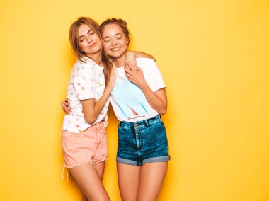 Trendy yaz giysileri iki genç güzel gülümseyen hipster kız. Seksi kaygısız kadınlar stüdyoda sarı duvar yakınında poz. Pozitif modeller deli gidiyor ve eğleniyor. Sarılma