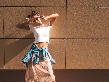 Boynuzları saç modeli ile güzel gülümseyen model yaz hipster beyaz t-shirt giysiler giymiş. Seksi kaygısız kız duvara yakın sokakta poz. Trendy komik ve pozitif kadın güneş gözlüğü eğlenmek