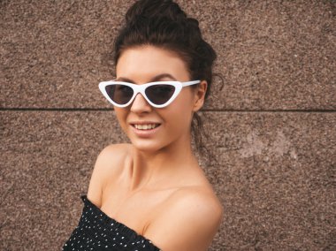 Güzel model zarif yazlık giysiler giymiş. Seksi kaygısız kız duvara yakın sokakta poz. Güneş gözlüğü trendy modern iş kadını eğlenmek