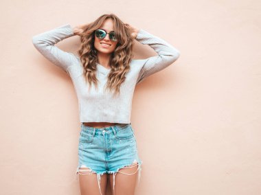 Yaz hipster kot şort giysiler giymiş güzel gülümseyen model Portresi. Duvara yakın sokakta poz veren modaya uygun kız. Komik ve pozitif kadın güneş gözlüğü eğlenmek
