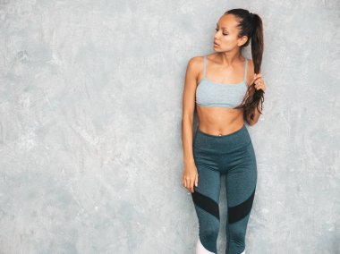 Spor kıyafetleri içindeki spor elbiseli kadın portresi. Spor giyimli genç bir bayan. Mükemmel bronzlaşmış vücutlu güzel bir manken. Stüdyoda Gray wal yakınlarında poz veren bir kadın.