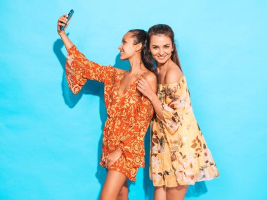 Yaz hippi elbiseli iki genç gülümseyen hippi kadın. Stüdyoda mavi duvarın yanında poz veren mankenler. Yüzünde olumlu duygular gösteren bir kadın.