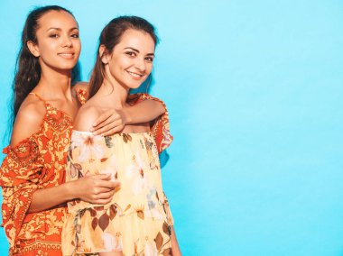 Son moda yaz kıyafetleri içinde gülümseyen iki genç hippi kız. Mavi duvarın yanında poz veren kaygısız kadınlar. Eğleniyor ve sarılıyorlar. Modeller iyi bir ilişki gösterir. Makyajsız bir kadın