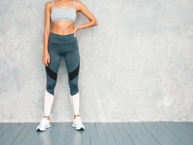 Spor kıyafetleri içindeki spor elbiseli kadın portresi. Spor giyimli genç bir bayan. Mükemmel bronzlaşmış vücutlu güzel bir manken. Stüdyoda gri duvarın yanında poz veren bir kadın.