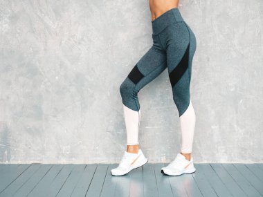 Spor kıyafetleri içindeki spor elbiseli kadın portresi. Spor giyimli genç bir bayan. Mükemmel bronzlaşmış vücutlu güzel bir manken. Stüdyoda gri duvarın yanında poz veren bir kadın.