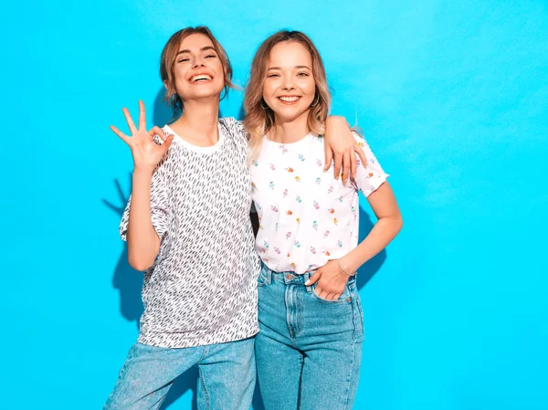 两个年轻美丽的金发嬉皮士女孩穿着时髦的夏天艳丽的T恤衫 在蓝色墙边摆姿势的无忧无虑的女人 有乐趣的正面模型 — 图库照片