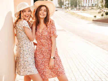 İki güzel, gülümseyen yeniyetme kız şık yaz kıyafetleri içinde. Sokakta şapkalarla poz veren kaygısız kadınlar. Pozitif modeller eğleniyor ve sarılıyorlar.
