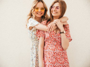 İki güzel gülümseyen yeniyetme kız şık yaz kıyafetleri içinde sokak arkasında güneş gözlükleriyle poz veren kaygısız kadınlar. Pozitif modeller eğleniyor ve sarılıyorlar.