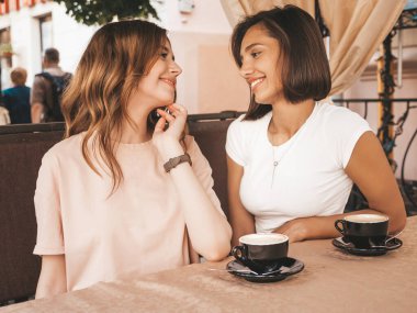 İki güzel, güler yüzlü yeniyetme yaz elbisesi giymiş iki genç kız. Kaygısız kadınlar veranda kafede sohbet edip kahve içiyor. Pozitif mankenler eğleniyor ve iletişim kuruyor.