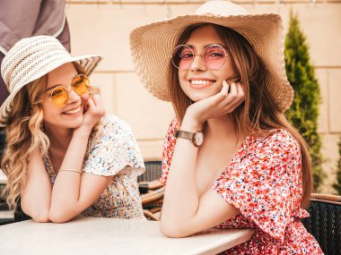 İki güzel, güler yüzlü yeniyetme yaz elbisesi giymiş iki genç kız. Veranda kafesinde güneş gözlükleriyle sohbet eden kaygısız kadınlar. Pozitif modeller eğleniyor ve iletişim kuruyor.
