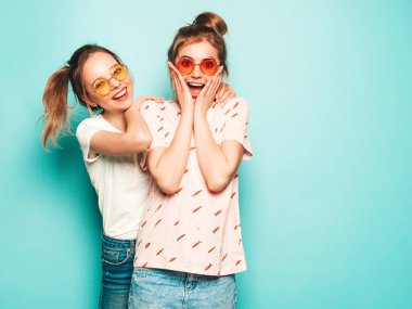 İki güzel sarışın, gülümseyen yenilikçi kız, son moda hippi kot pantolon giyiyorlar. Mavi duvarın yanında poz veren kaygısız seksi kadınlar. Moda ve pozitif modeller güneş gözlükleriyle eğleniyor.