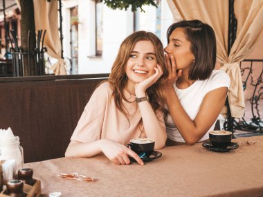 Son moda yaz kıyafetleri içinde iki güzel gülümseyen hippi kız. Kaygısız kadınlar veranda kafede sohbet edip kahve içiyorlar. Pozitif model, arkadaşının kulağına verdiği sırrı paylaşıyor.
