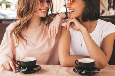 Son moda yaz kıyafetleri içinde iki güzel gülümseyen hippi kız. Kaygısız kadınlar veranda kafede sohbet ediyor ve kahve içiyor. Pozitif modeller eğleniyor ve iletişim kuruyor.