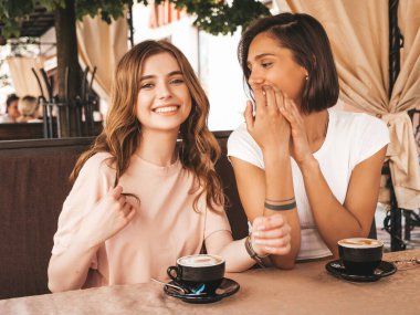 Son moda yaz kıyafetleri içinde iki güzel gülümseyen hippi kız. Kaygısız kadınlar veranda kafede sohbet ediyor ve kahve içiyor. Pozitif modeller eğleniyor ve iletişim kuruyor.