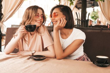 Son moda yaz kıyafetleri içinde gülümseyen iki genç hippi kız. Veranda kafesinde sohbet eden ve kahve içen kaygısız kadınlar. Pozitif modeller eğleniyor ve iletişim kuruyor.
