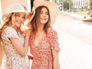 İki güzel gülümseyen yeniyetme kız şık yaz kıyafetleri içinde sokakta şapkalarla poz veren kaygısız kadınlar. Pozitif modeller eğleniyor ve sarılıyorlar.