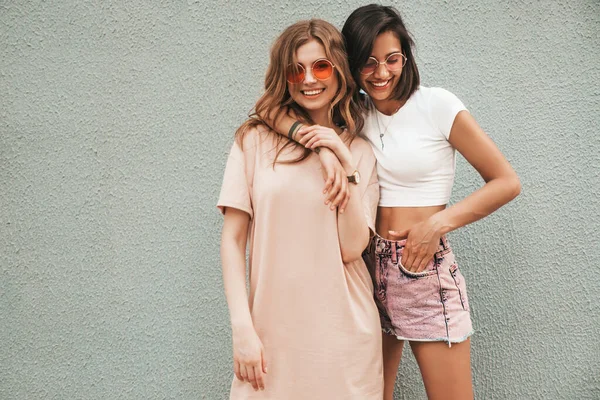 两个穿着时髦夏装的年轻漂亮的嬉皮士女孩 戴着太阳镜在街上摆出一副无忧无虑的性感女人的模样 有乐趣和拥抱的正面模型 — 图库照片