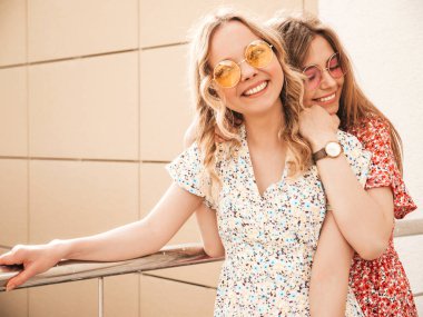 İki güzel gülümseyen yeniyetme kız şık yaz kıyafetleri içinde sokakta güneş gözlükleriyle poz veren kaygısız kadınlar. Pozitif modeller eğleniyor ve deliriyor.