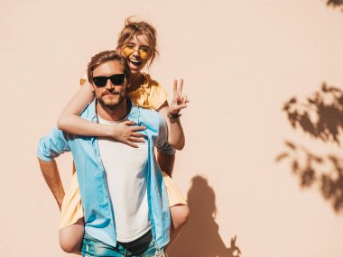 Gülümseyen güzel kız ve yakışıklı erkek arkadaşının portresi. Gündelik yazlık elbiseli kadın ve kot pantolonlu erkek. Mutlu, neşeli bir aile. Kadın duvarın yanında eğleniyor.