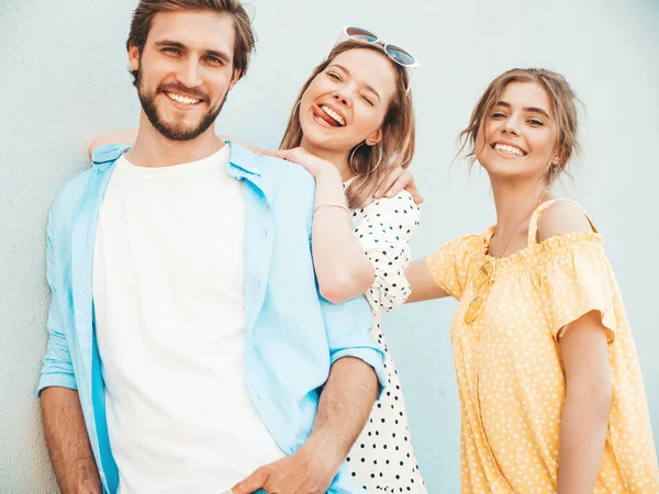 stock image Group of young three stylish friends posing in the street. Fashion man and two cute girls dressed in casual summer clothes. Smiling models having fun near wall.Cheerful women and guy outdoors