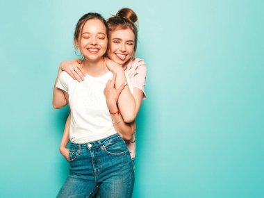 İki güzel sarışın, gülümseyen yenilikçi kız, son moda hippi kot pantolon giyiyorlar. Mavi duvarın yanında poz veren kaygısız seksi kadınlar. Moda ve pozitif modeller eğleniyor.