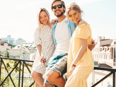 Sokakta poz veren üç genç arkadaş grubu. Moda adamı ve sıradan yaz kıyafetleri giymiş iki tatlı kız. Gülümseyen modeller güneş gözlükleriyle eğleniyorlar. Neşeli kadınlar ve açık hava adamı.