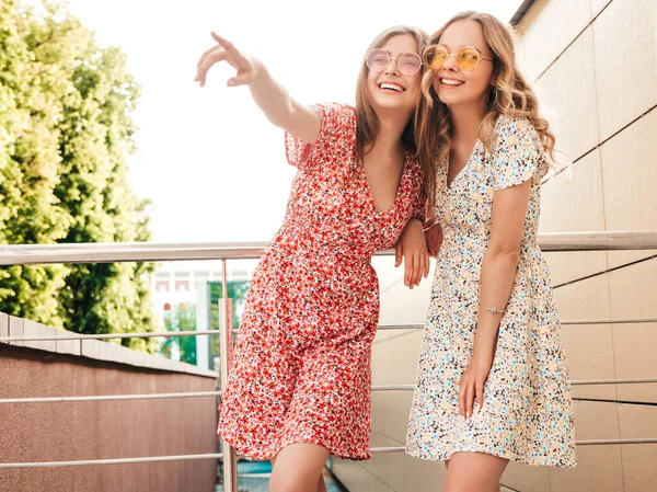 流行の夏の太陽の下で2人の若い美しい笑顔のヒップスターの女の子 サングラスで通りの背景にポーズセクシーな屈託のない女性 何か面白いことを指差している肯定的なモデル — ストック写真