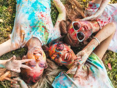 Yaz mevsiminde Holi Renk Festivali 'nde parti veren üç mutlu güzel kız. Gün batımında müzik etkinliği sonrasında gülümseyen genç bayan arkadaşlar. Güneş gözlüğüyle çimlerin üzerinde yatan mankenler.