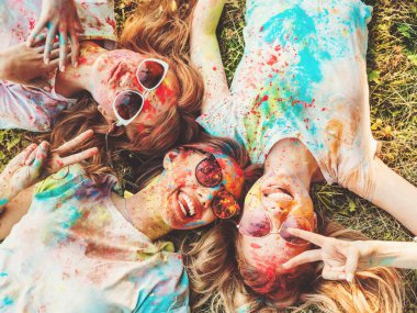 Yaz mevsiminde Holi Renk Festivali 'nde parti veren üç mutlu güzel kız. Gün batımında müzik etkinliği sonrasında gülümseyen genç bayan arkadaşlar. Güneş gözlüğüyle çimlerin üzerinde yatan mankenler.