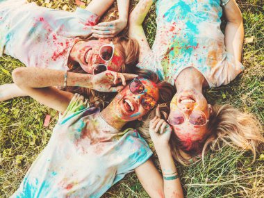 Yaz mevsiminde Holi Renk Festivali 'nde parti veren üç mutlu güzel kız. Gün batımında müzik etkinliği sonrasında gülümseyen genç bayan arkadaşlar. Güneş gözlüğüyle çimlerin üzerinde yatan mankenler.