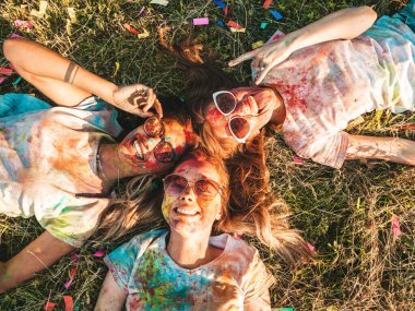 Yaz mevsiminde Holi Renk Festivali 'nde parti veren üç mutlu güzel kız. Gün batımında müzik etkinliği sonrasında gülümseyen genç bayan arkadaşlar. Güneş gözlüğüyle çimlerin üzerinde yatan mankenler.