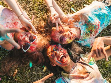 Yaz mevsiminde Holi Renk Festivali 'nde parti veren üç mutlu güzel kız. Gün batımında müzik etkinliği sonrasında gülümseyen genç bayan arkadaşlar. Güneş gözlüğüyle çimlerin üzerinde yatan mankenler.
